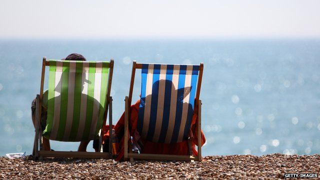 Two people sit on deckchairs on the beach