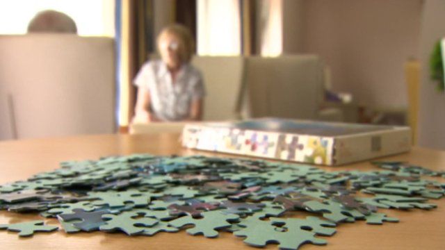 Jigsaw in foreground with older people on chair out of focus in the background