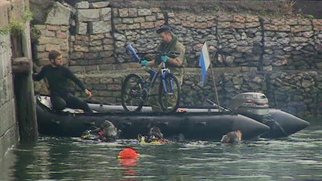 Two men in an inflatable boat pull a bicycle out of the harbour