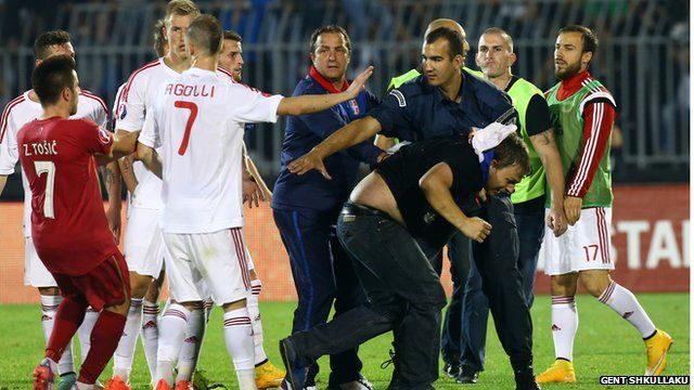 A policeman escorts a Serbian fan that invaded the pitch after a flag with Albanian national symbols was flown by a remotely operated drone during the UEFA Euro 2016 group I qualifying football match between Serbia and Albania in Belgrade on October 14, 2014
