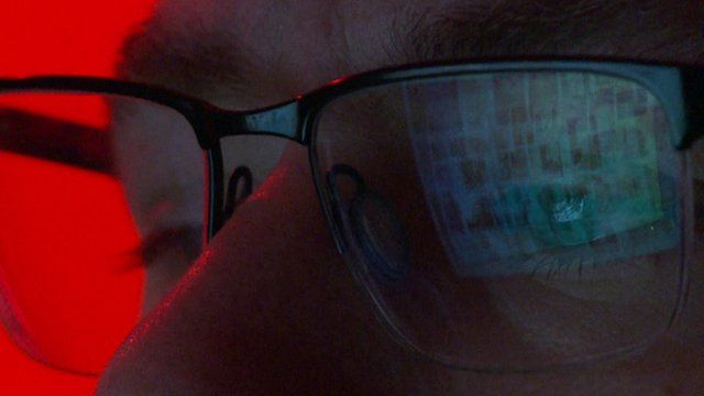 Close up of face of man in glasses with computer images reflected in lenses