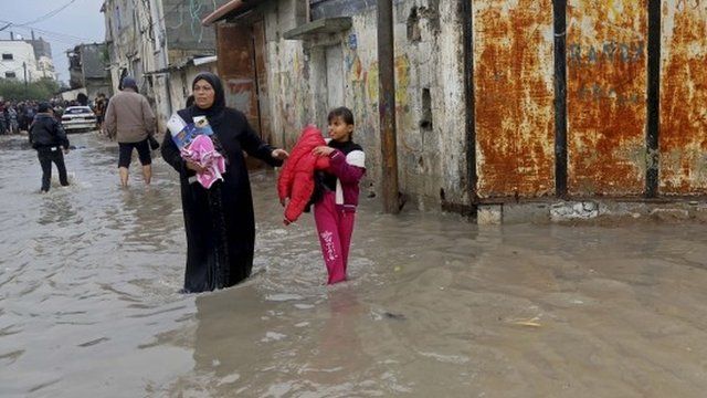 A Palestinian woman and her daughter carry their belongings from their flooded family house