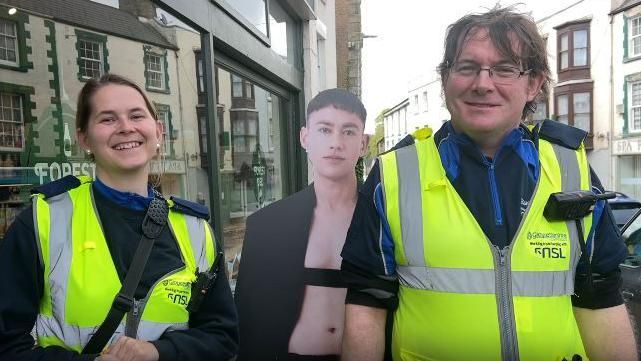 Two traffic wardens standing next to a cardboard cutout of Olly Alexander