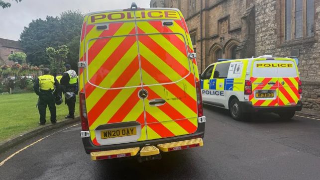 The back of two police vans parked outside a church. There are also two officers standing beside the vehicles, wearing hi-vis uniforms and carrying helmets.