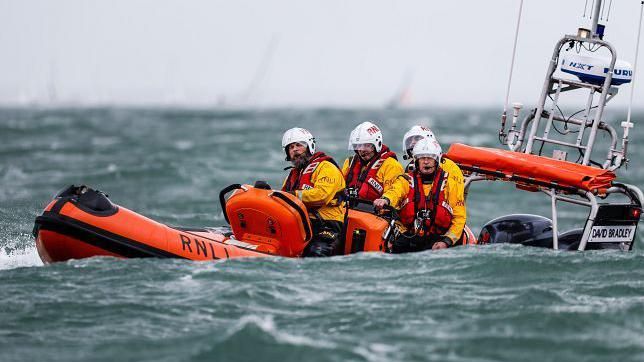 An RNLI lifeboat crew out on the sea in an orange lifeboat with all crew members wearing yellow jackets, life vests and helmets