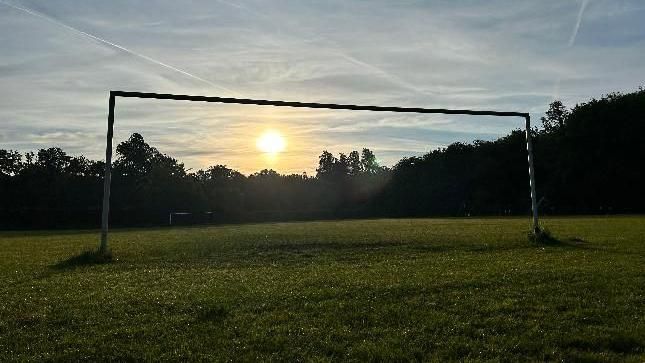 A field and a goal post with the sun coming through it 