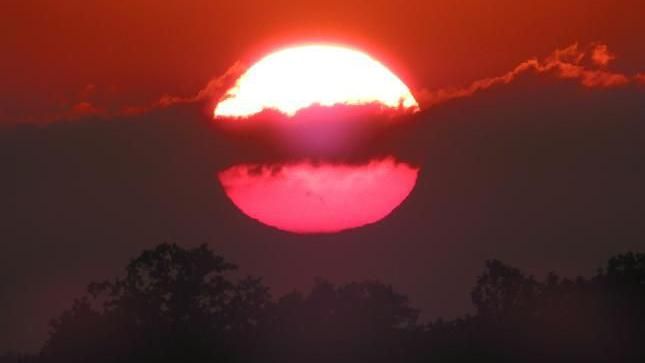 A red sun with clouds positioned in front slicing it in half 