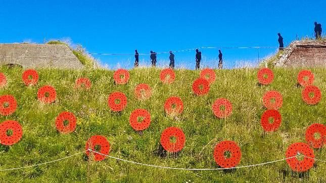 Poppies on a field with figures of soldiers on top of the hill