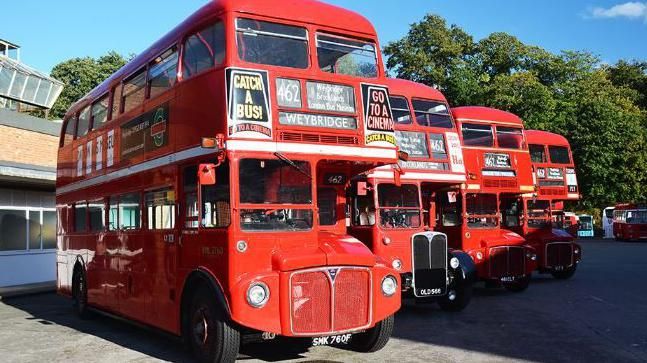 Four bright red heritage buses line up at an angle outside the London Bus Museum in Weybridge