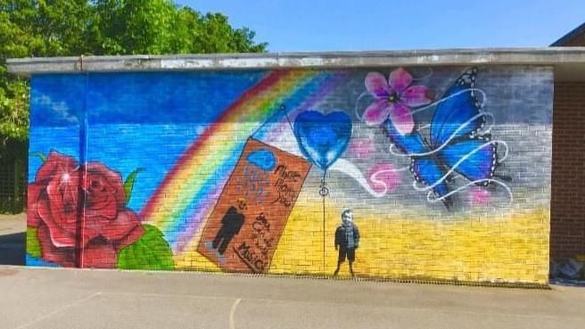 mural on a brick wall featuring a rainbow, a blue butterfly and a small black and white boy