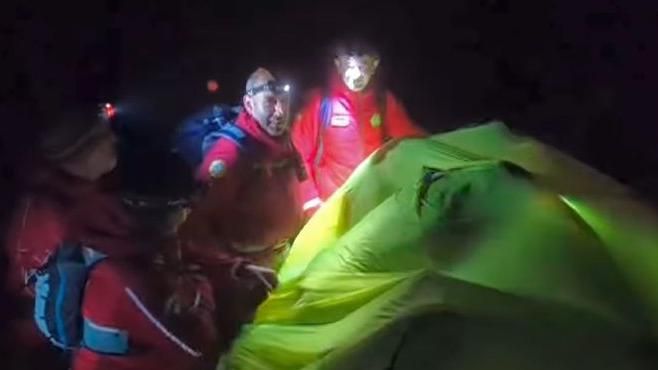 Rescuers in red jackets cover the walkers with a green tent to get warm