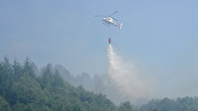 Вертолет сбрасывает воду на пламя возле свалки Брин Пика в Абердаре