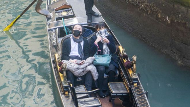 Туристы надевают защитные маски для лица во время посещения Венеции после отмены празднования Венецианского карнавала 24 февраля 2020 года в Венеции, Италия. Последние дни карнавала были отменены из-за вспышки коронавируса COVID-19 в Италии, в результате которого в стране погибло шесть человек.