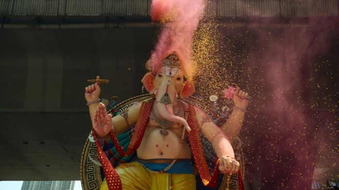 Индийские преданные заливают лепестки роз и цветной порошок огромному идолу индуистского божества со слонами во главе с Ганешой во время его шествия для погружения в Мумбаи 5 сентября 2017 года.