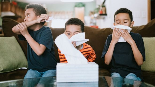Three boys are sick at home, coughing and sneezing into tissues.