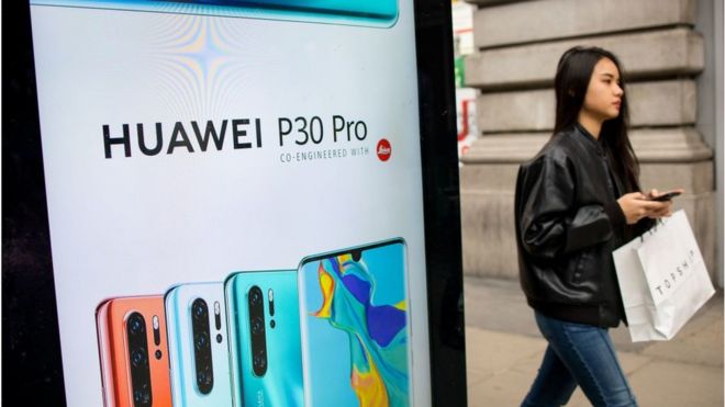 O femeie trece pe lângă o reclamă la o stație de autobuz pentru un smartphone Huawei din Londra