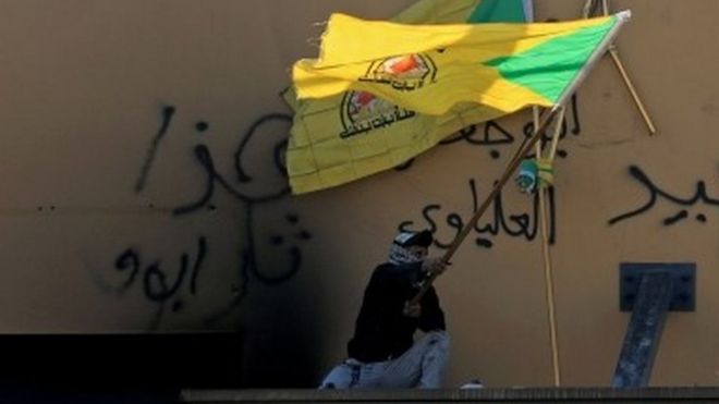 رجل يلوح بعلم كتائب حزب الله أمام السفارة الأمريكية في العراق
