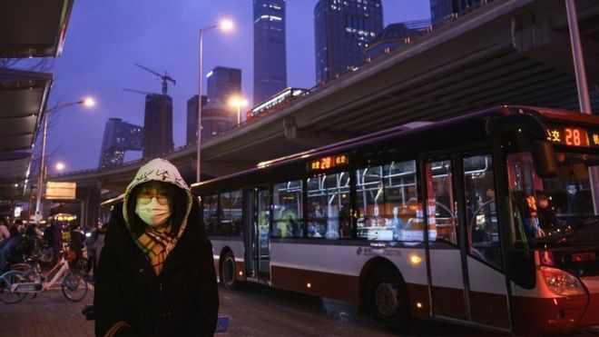 A Chinese office worker wears a protective mask as she waits to take a public bus after leaving work on 2 March 2020 in Beijing, China