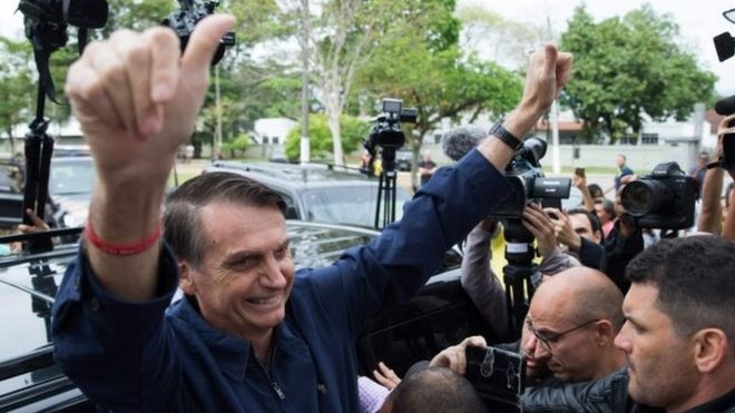 Jair Bolsonaro поднимает пальцы после того, как проголосовал на Villa Militar,