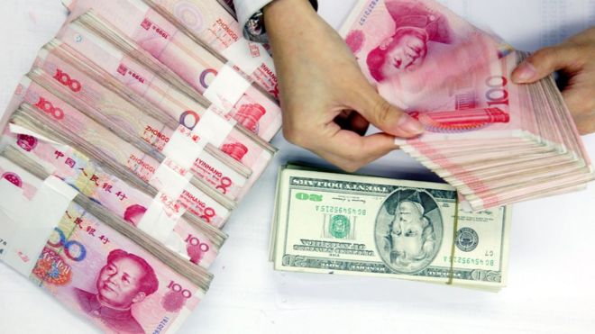 Служащий подсчитывает стопки китайских юаней и долларов США