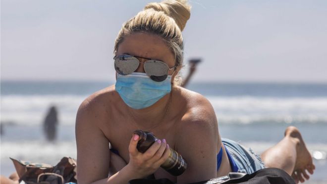 Женщина в маске загорает на пляже во время пандемии нового коронавируса в Калифорнии, 25 апреля 2020 г.