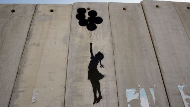 Trabalho de Banksy na parede que separa Israel mostra a silhueta de uma garota suspensa por com balões