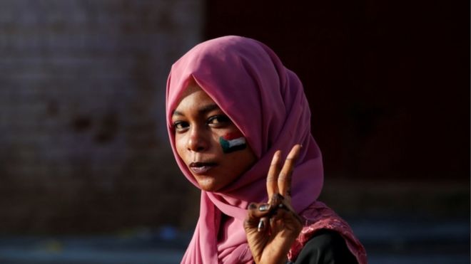Суданский протестующий держит два пальца в знак победы перед министерством обороны в Хартуме