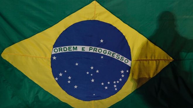 Sombra de um homem em frente a bandeira do Brasil exposta em manifestação
