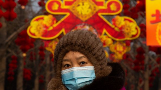 Женщина в маске идет под декорациями к Лунному Новому году в парке Дитан 26 января 2020 года в Пекине, Китай.
