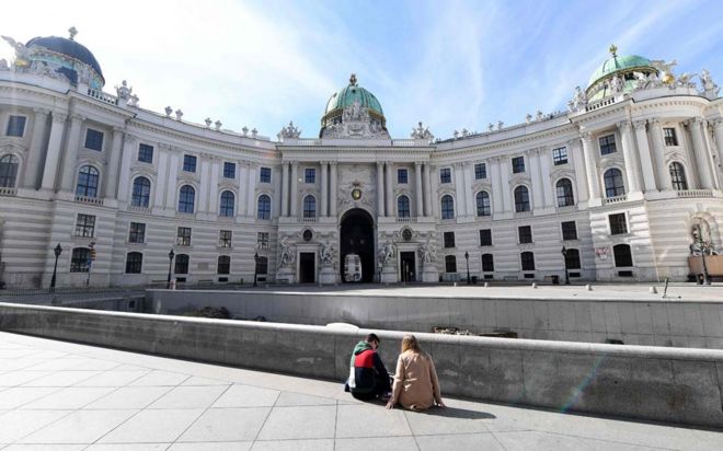 Duas pessoas sentam em uma praça vazia no centro de Viena.