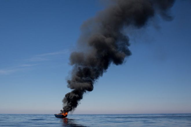 إضرام النار في قارب خشبي صغير يوم 18 مايو/أيار 2017 بعد إنقاذ اللاجئين والمهاجرين الذين كانوا على متنه في جزيرة لابيدوسا بإيطاليا.