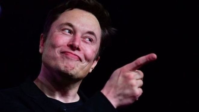 Retrato de Elon Musk com dedo em riste e sorriso sobre fundo preto