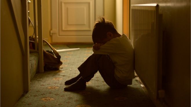 Мальчик сидит против радиатора в коридоре с опущенной головой