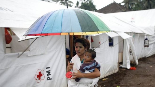 Женщина несет ребенка в лагере для людей, которые были эвакуированы из деревень вблизи вулкана Агунг (29 ноября 2017 г.)