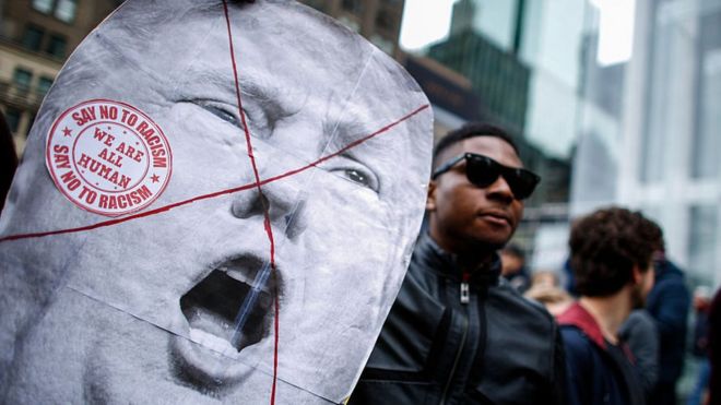 Un hombre negro sostiene una pancarta con la cara de Trump tachada con una equis