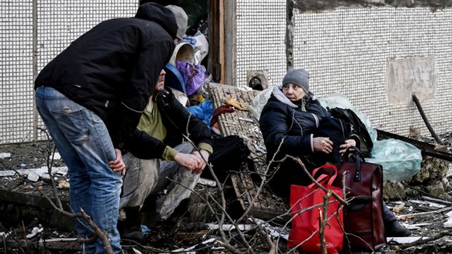 People stand outside a destroyed building after bombings on the eastern Ukraine town of Chuhuiv on February 24, 2022