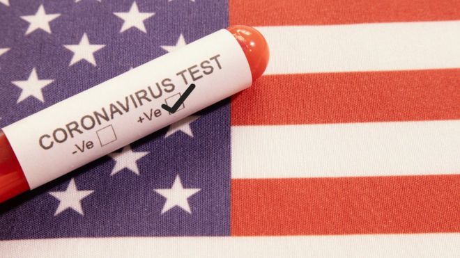 Tubo com papel registrando positivo para 'Teste de coronavírus' em cima de bandeira dos EUA