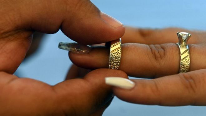 A groom puts a ring on the finger of his bride during a mass wedding
