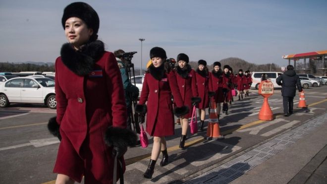 Северокорейские болельщики пересекают автостоянку после прибытия в составе делегации