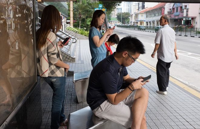 Пассажиры отправляют SMS-сообщения на свой мобильный телефон во время ожидания общественного транспорта в Balestier Road, Сингапур