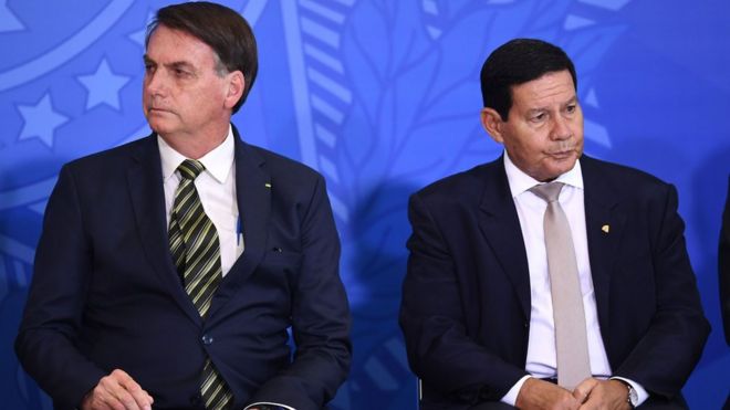 Bolsonaro e Mourão sentados, olhando para lados opostos, em evento