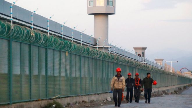 Workers walk by the perimeter fence of what is officially known as a vocational skills education centre in Dabancheng in Xinjiang in September 2018