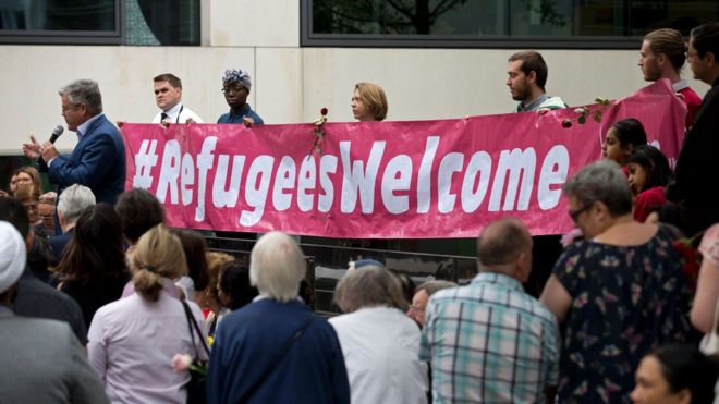 Люди держат плакат с надписью «Добро пожаловать беженцам»