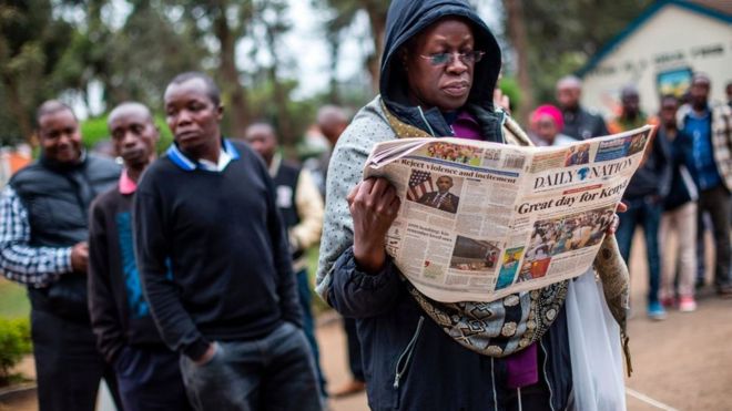 A man reads a newspaper with the headline 'Great day for Kenya' while waiting to cast their ballot in the general elections at a polling station in Kilimani Primary School, Nairobi, Kenya, on August 8, 2017 during the nationwide elections