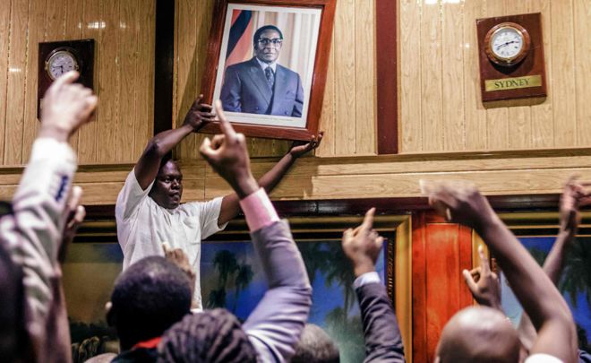 Люди снимают со стены в Международном конференц-центре, где заседал парламент, портрет бывшего президента Зимбабве Роберта Мугабе после его отставки 21 ноября 2017 года в Хараре.