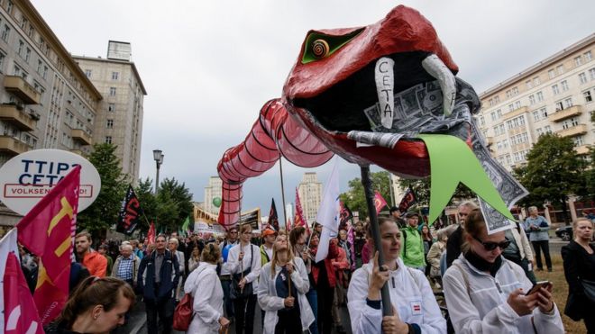 Протестующие держат гигантскую змею с долларовыми банкнотами во рту, чтобы протестовать против соглашений о свободной торговле TTIP и CETA с гигантской марионеткой 17 сентября 2016 года в Берлине, Германия.