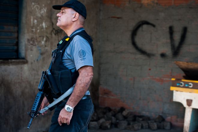 : Патруль бразильской военной полиции с символом в нижней части преступной группы Командо Вермелу после входа 30 марта 2014 года в Рио-де-Жанейро, Бразилия, в неуказанный комплекс «да Маре», один из крупнейших комплексов «фавела» в Рио-де-Жанейро.