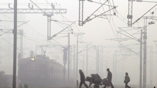 Носильщик несет багаж пассажира, когда местный поезд прибывает среди утреннего тумана на железнодорожную станцию ??Низамуддин в Нью-Дели, Индия, в пятницу, 2 января 2004 года.
