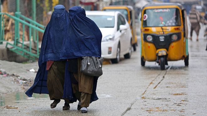 Afghan burqa-clad women walk along a street on a rainy day in Jalalabad on January 22, 2023