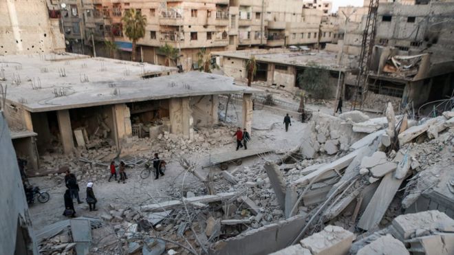 Сирийцы проходят мимо разрушенных зданий в Арбине, в Восточной Гуте за пределами Дамаска, Сирия (27 ноября 2017 года)